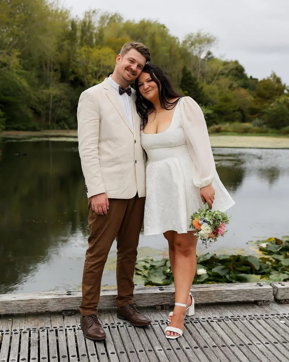 A newly married couple cuddled up on a jetty beside a lake