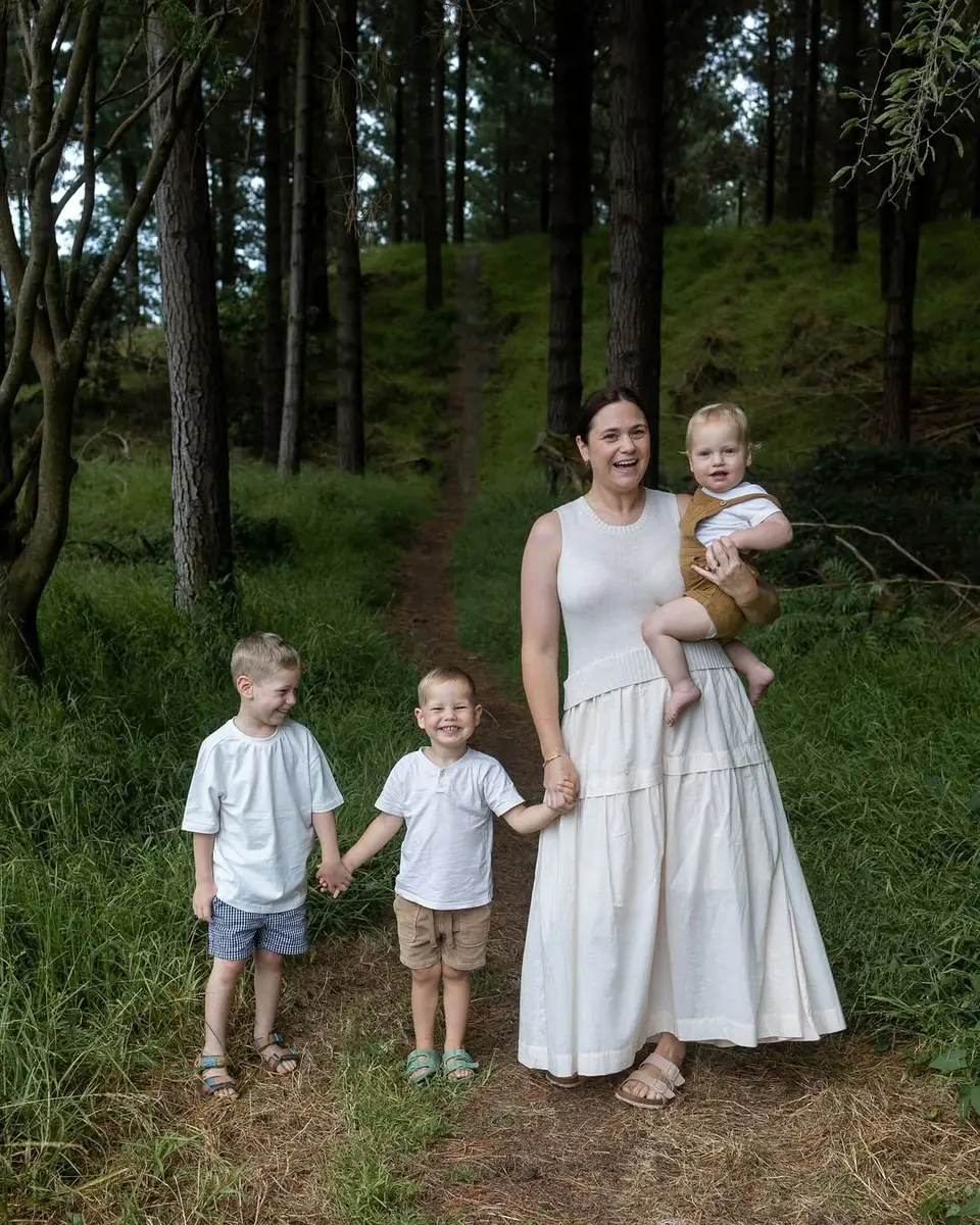 A mum carrying her baby while her two young boys walk hand in hand down a forest track